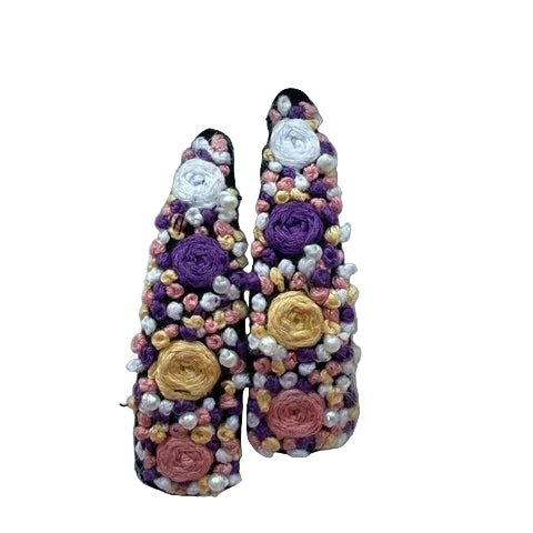 A pair of pointed-toe flats decorated with purple, pink, and gold fabric flowers and white pearl-like beads, displayed on a white faux fur background.